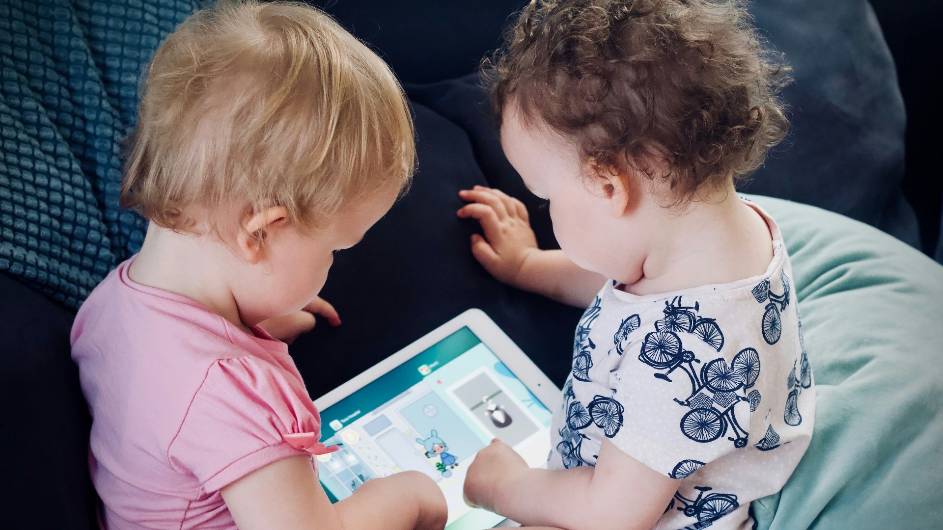 two toddlers sitting on sofa while using tablet computer