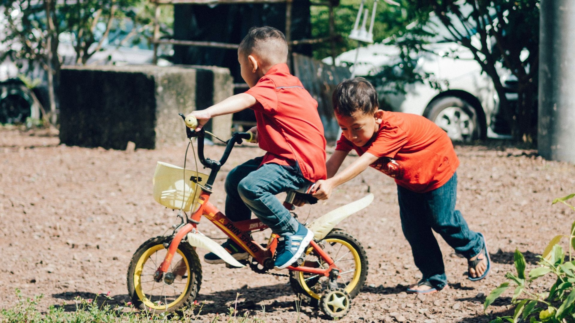 boy in orange t-shirt riding on bicycle during daytime