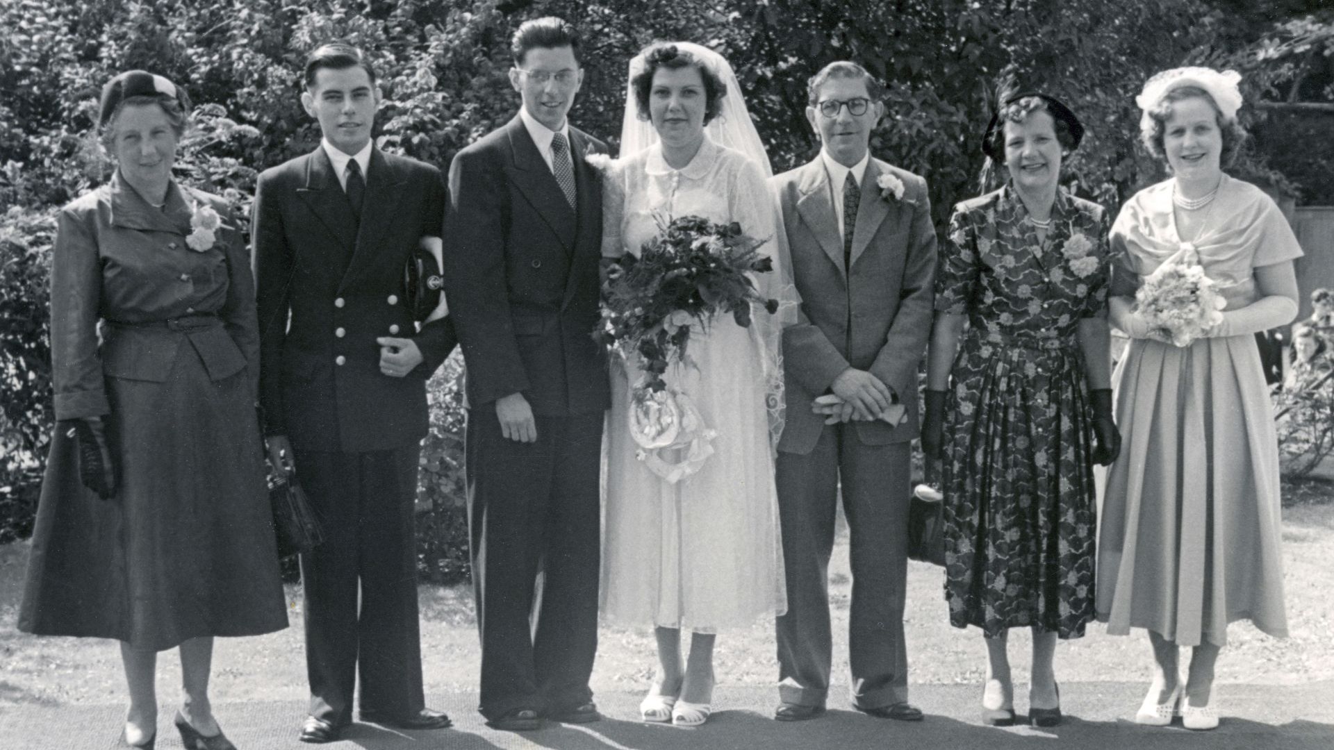 grayscale photo of man in black suit jacket standing between 2 women