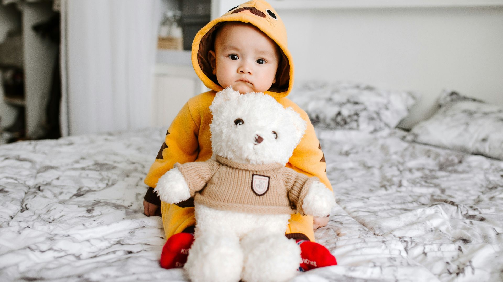 toddler sitting on bed beside white bear plush toy