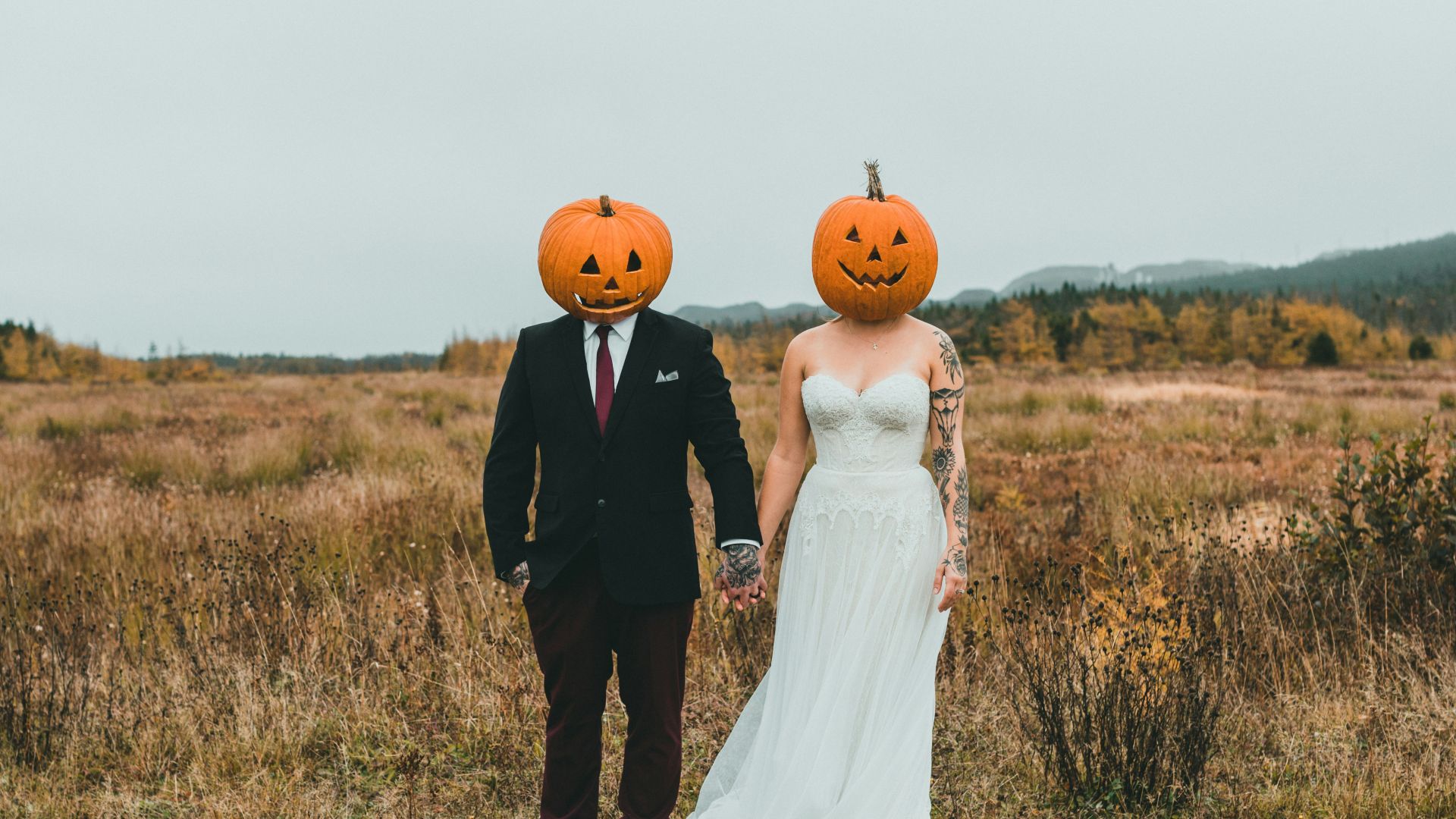 a bride and groom wearing pumpkin heads in a field