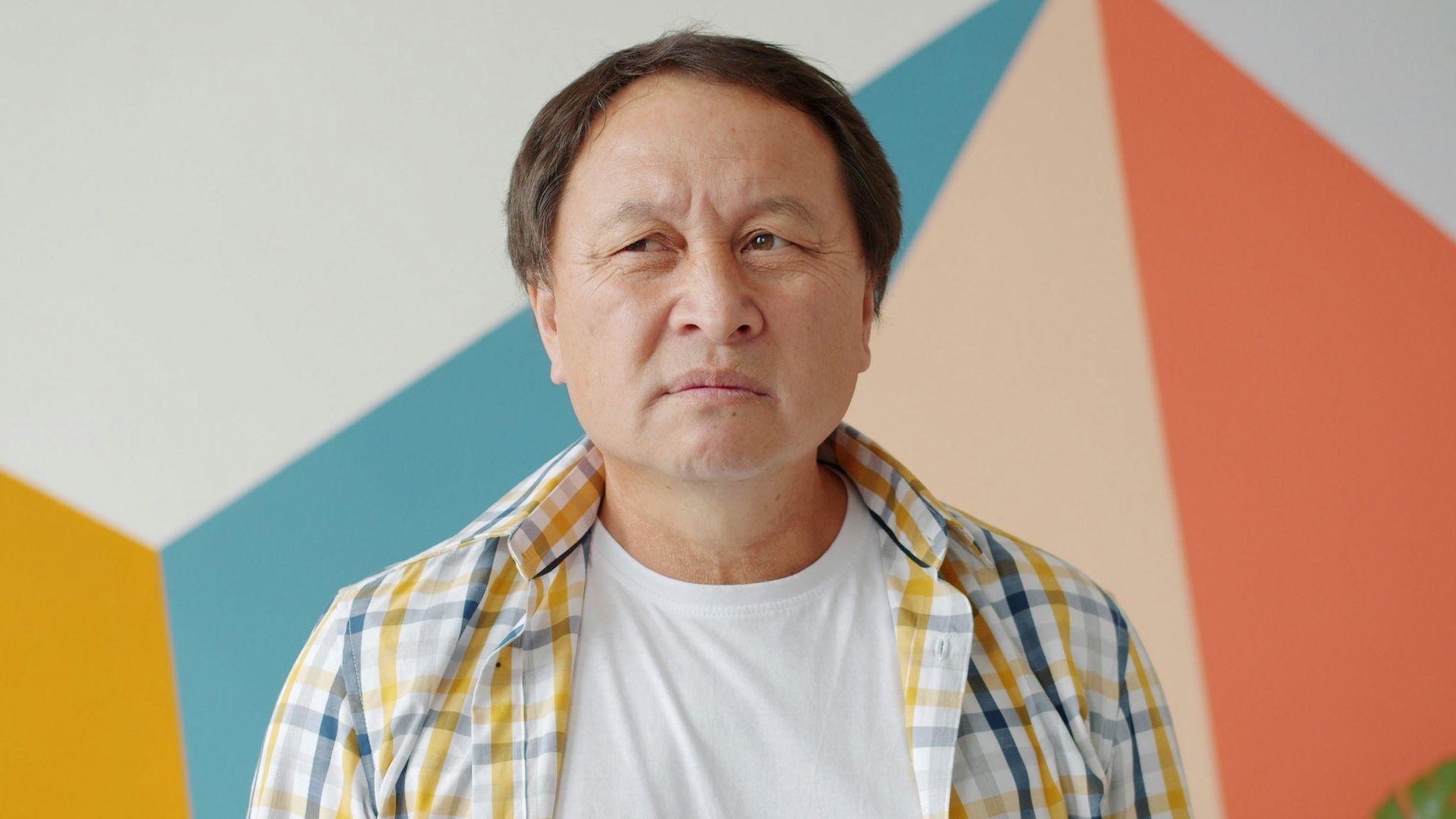 Man in plaid shirt stands against colorful geometric wall