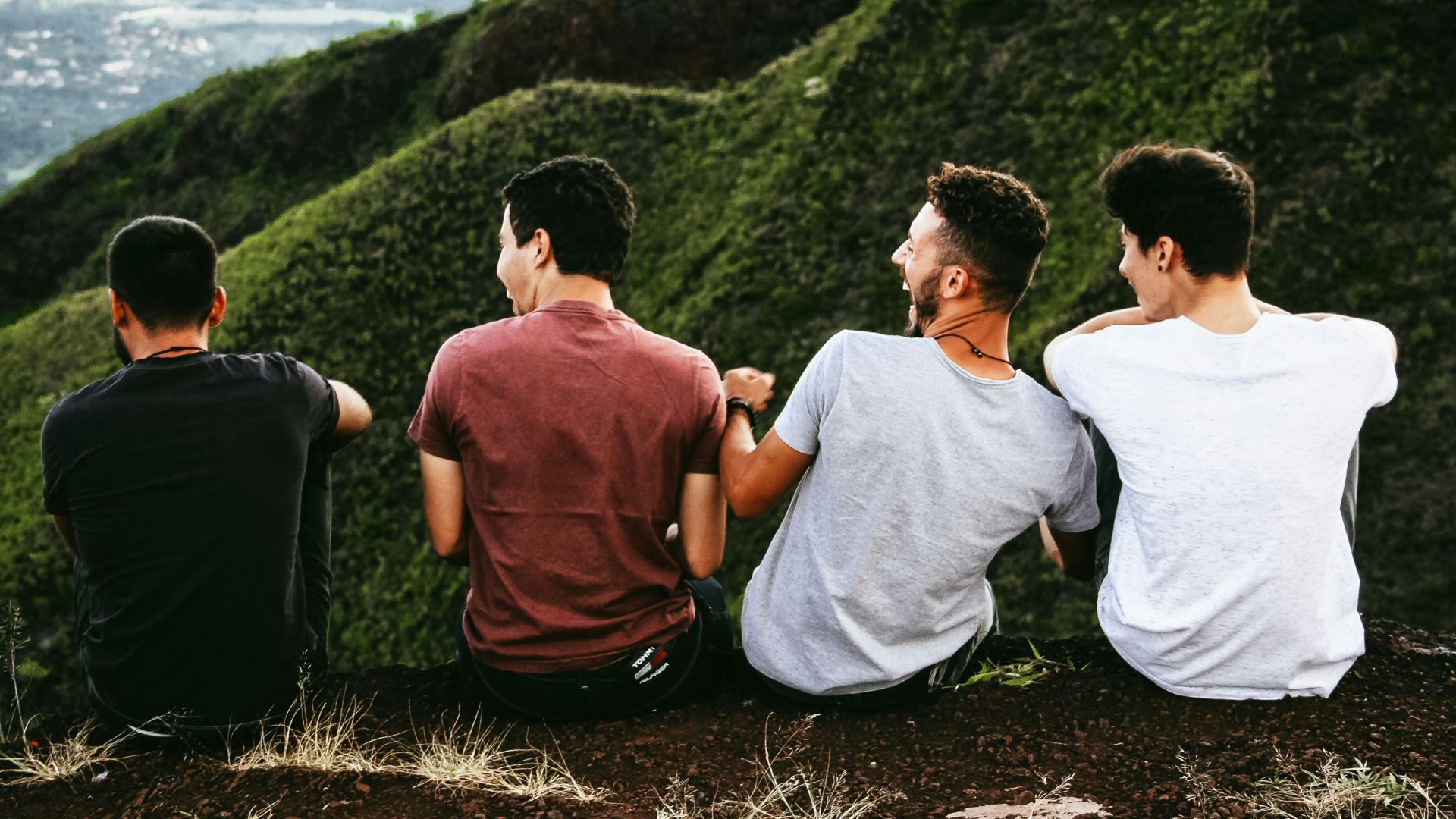 row of four men sitting on mountain trail
