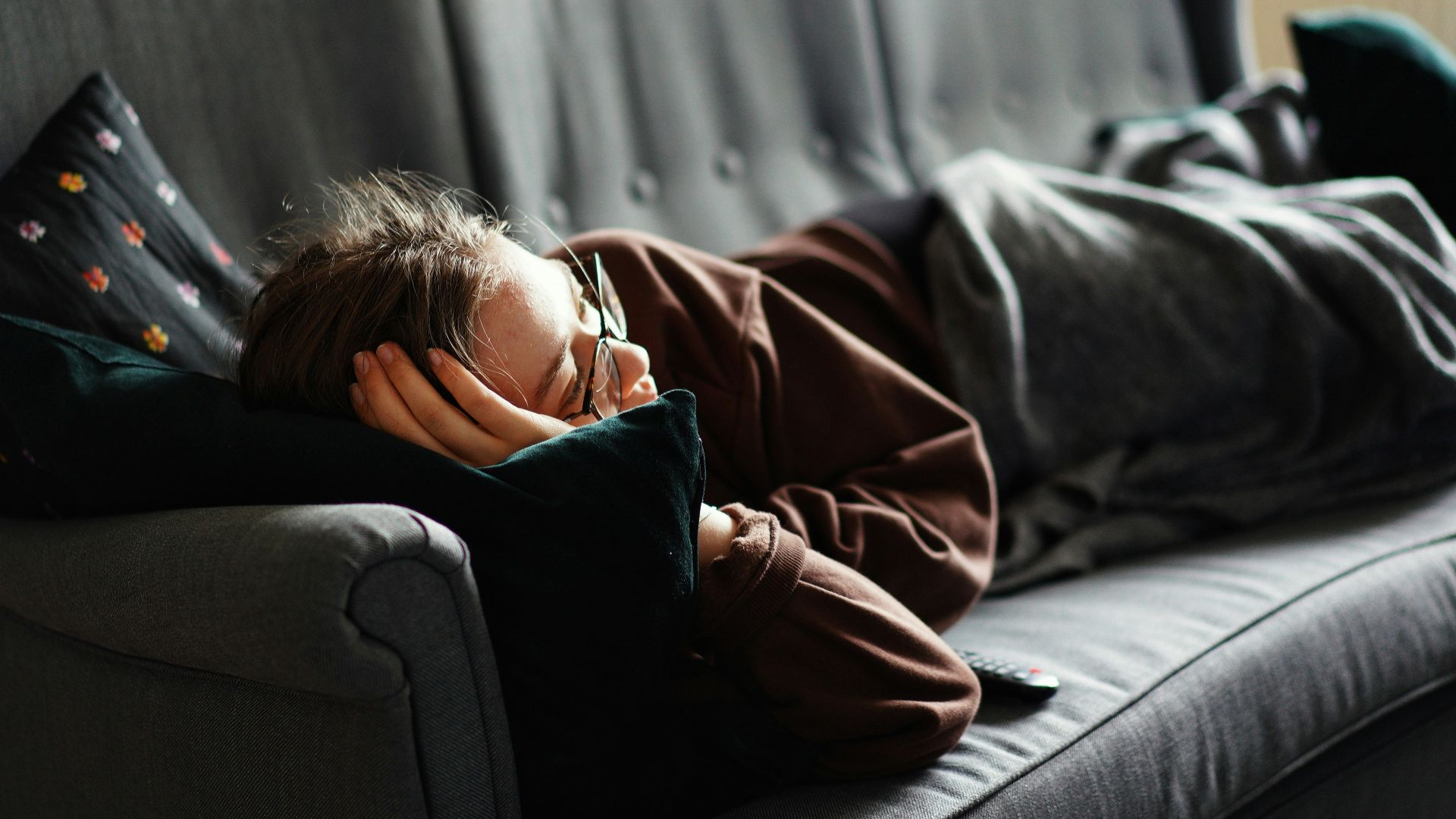 woman in pink jacket lying on gray couch