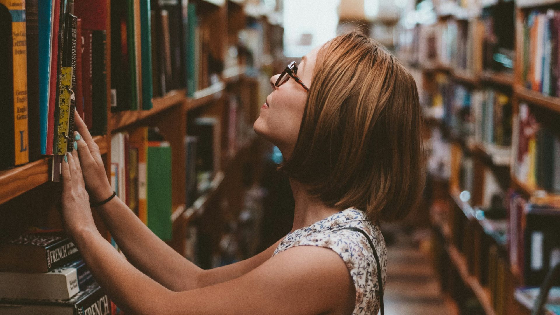 woman standing between library book shelves