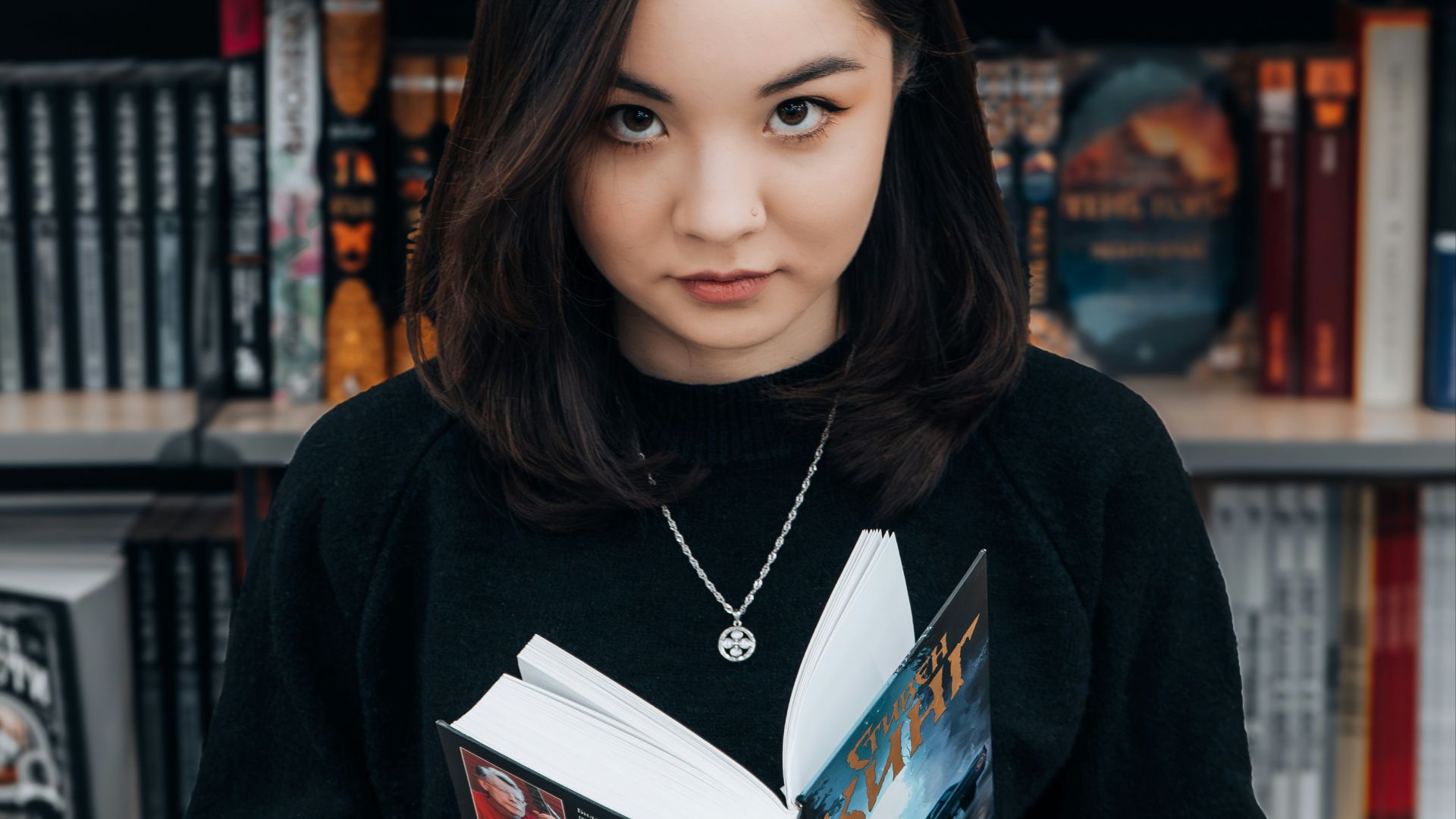 a woman standing in front of a bookshelf holding a book