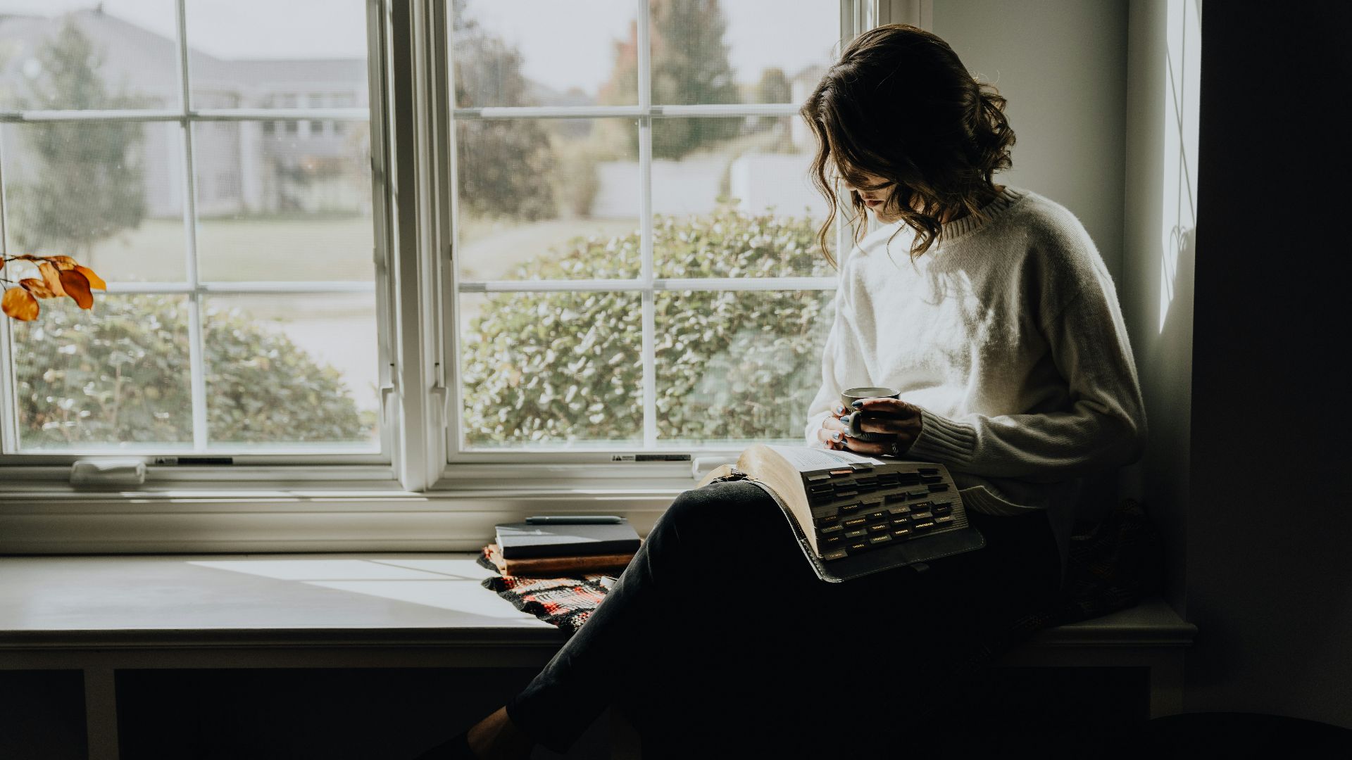 A woman sitting on a window sill reading a book