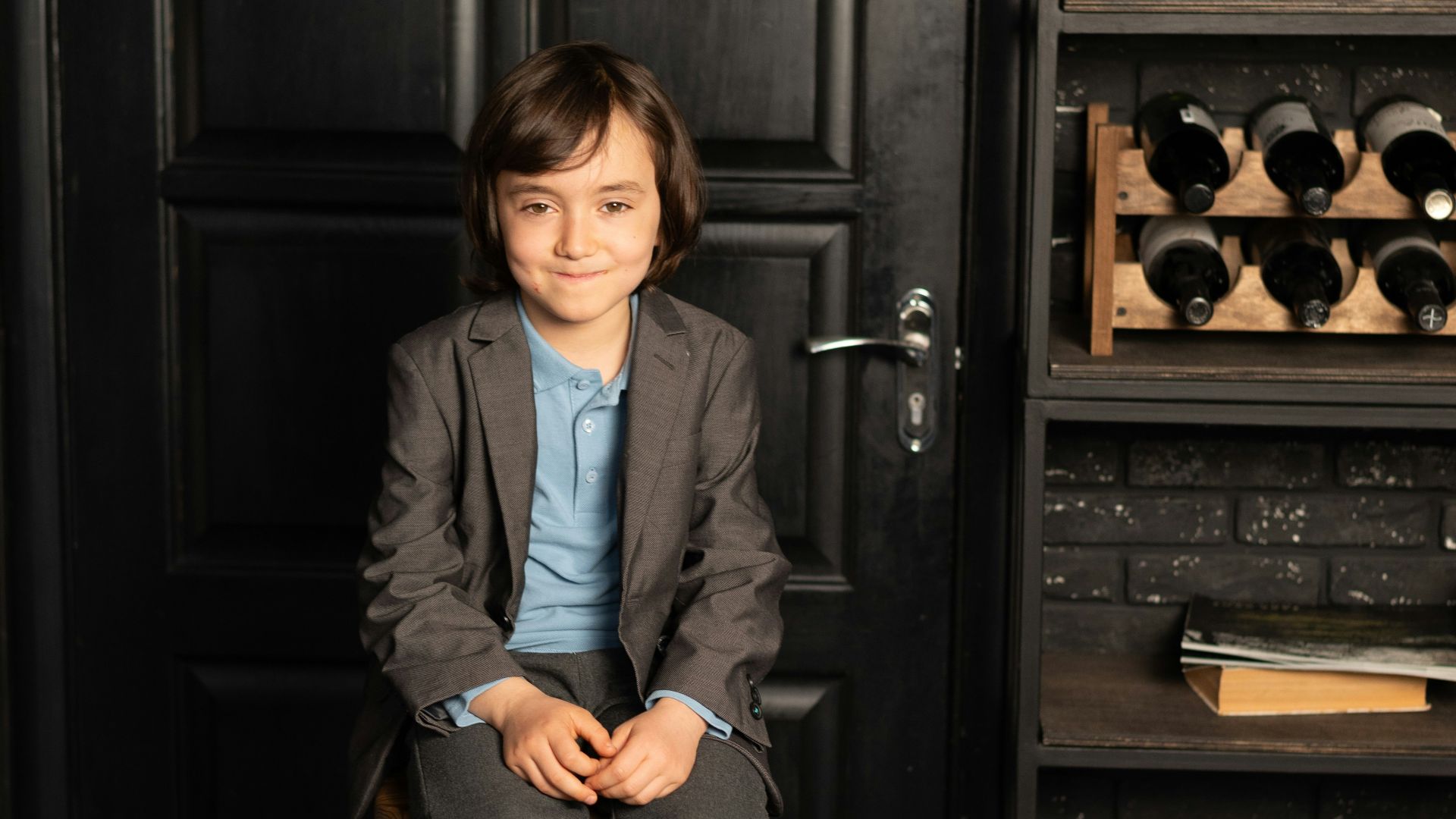 a young boy sitting on a stool in front of a black door