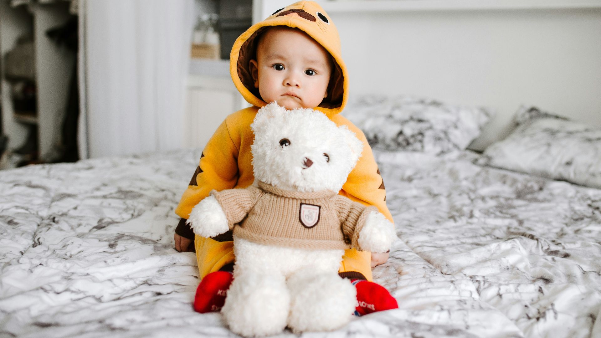 toddler sitting on bed beside white bear plush toy