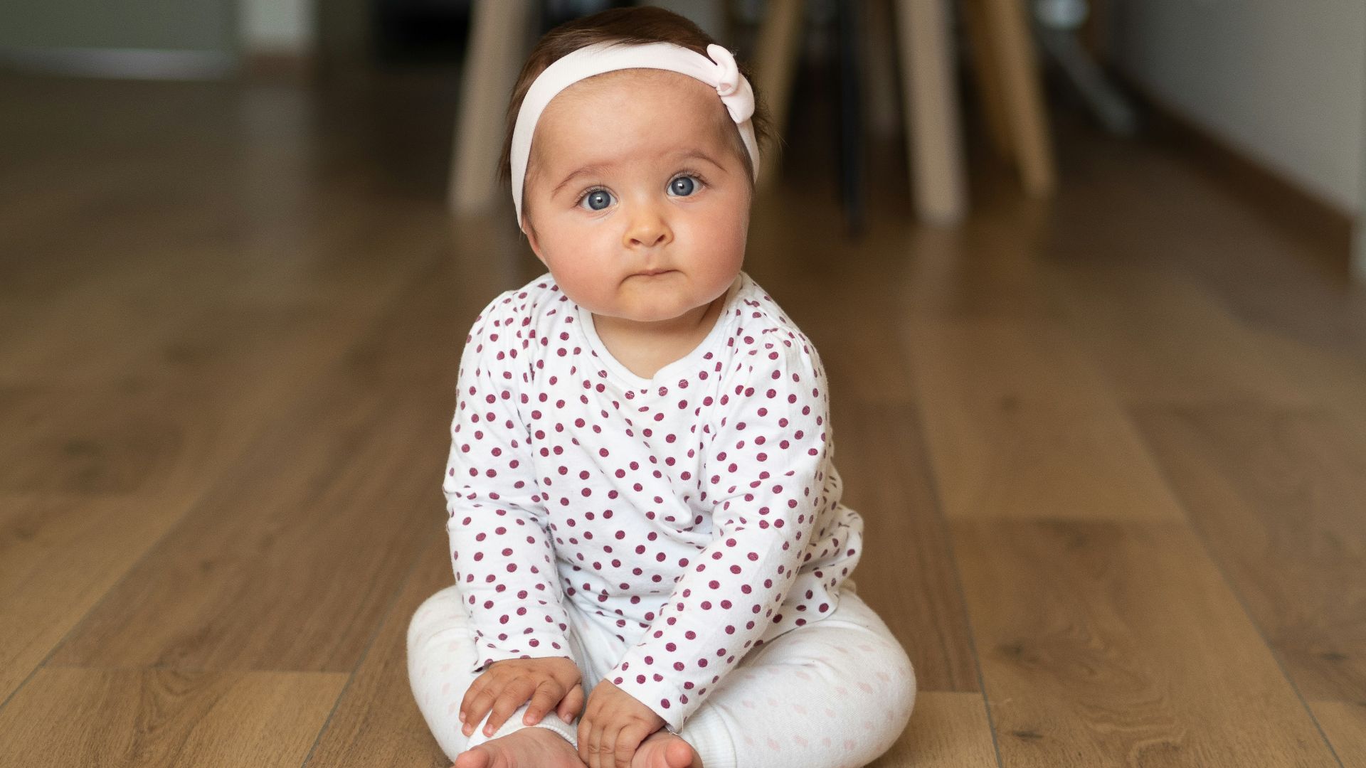 baby in white and black onesie lying on brown wooden floor