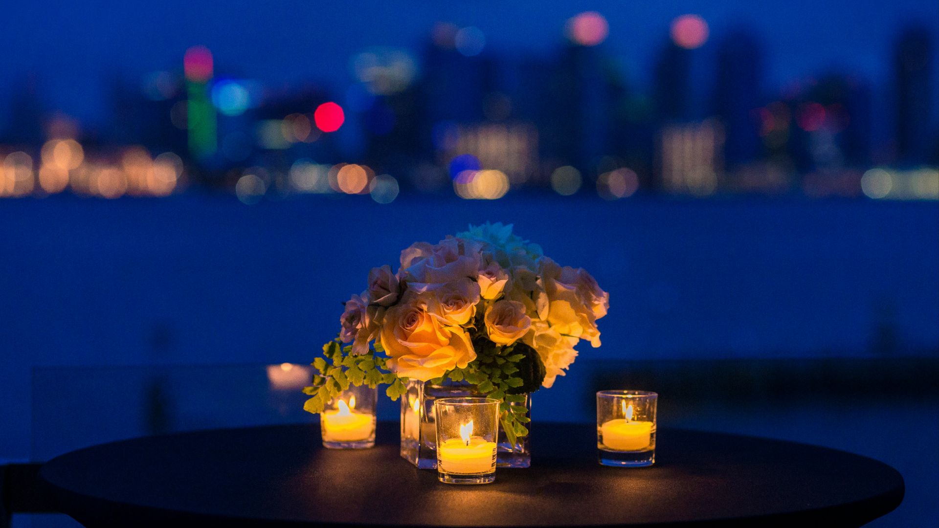 white rose bouquet in vase with three tealight candle votives on round brown wooden table