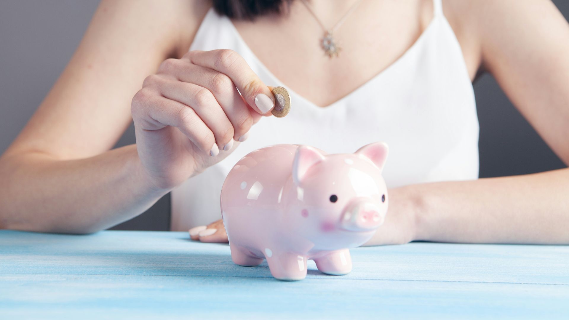 woman in white tank top holding pink pig figurine