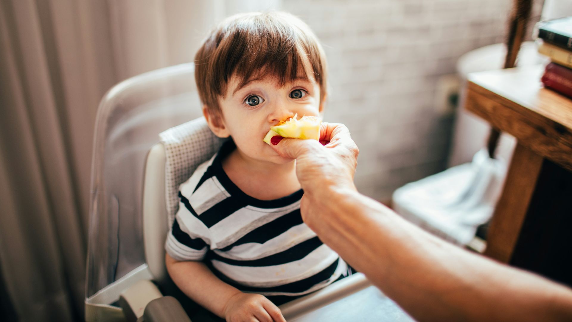 boy in black and white stripe shirt eating yellow fruit sitting on white sofa