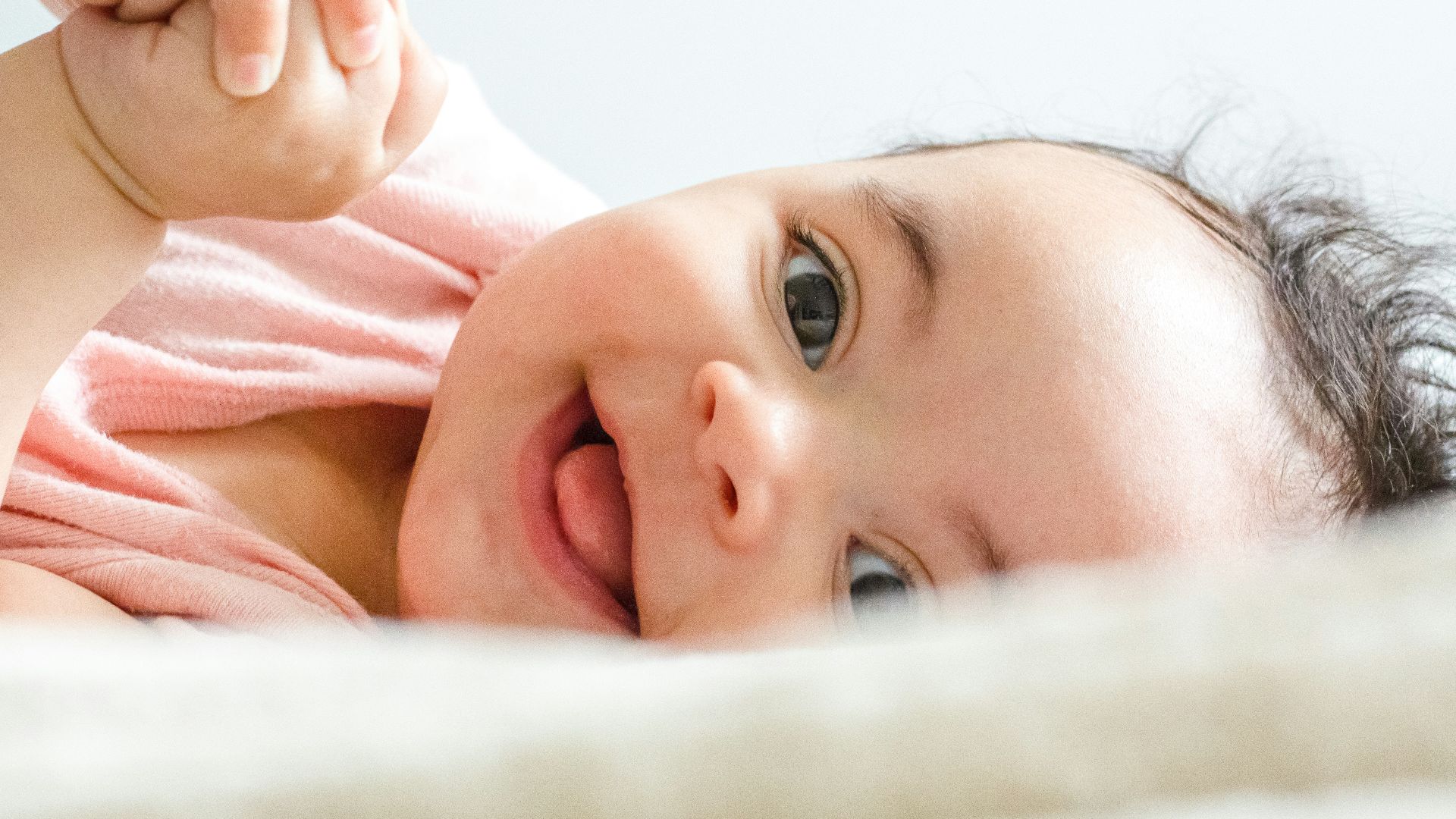 baby in pink shirt lying on white textile
