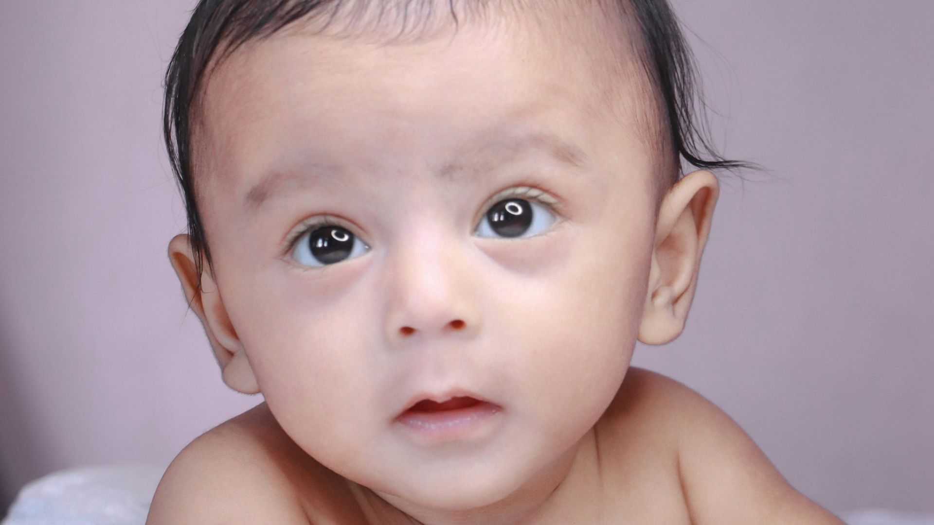 topless baby lying on white textile