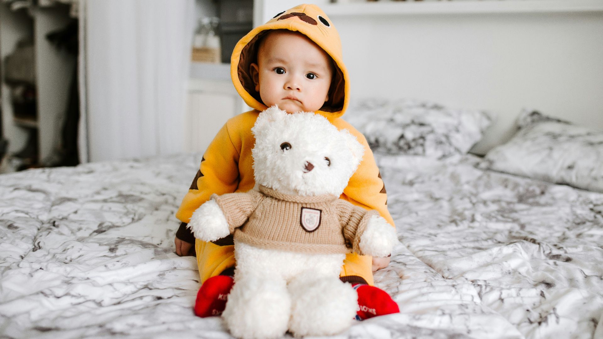 toddler sitting on bed beside white bear plush toy