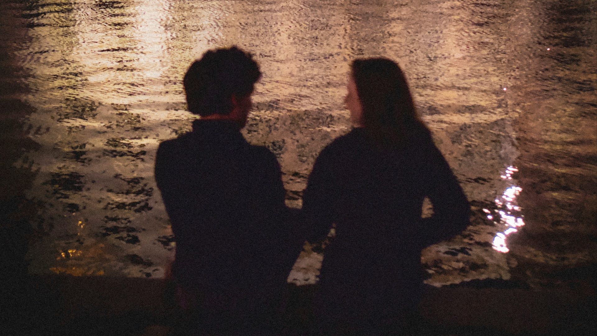 silhouette of man and woman standing beside body of water during night time