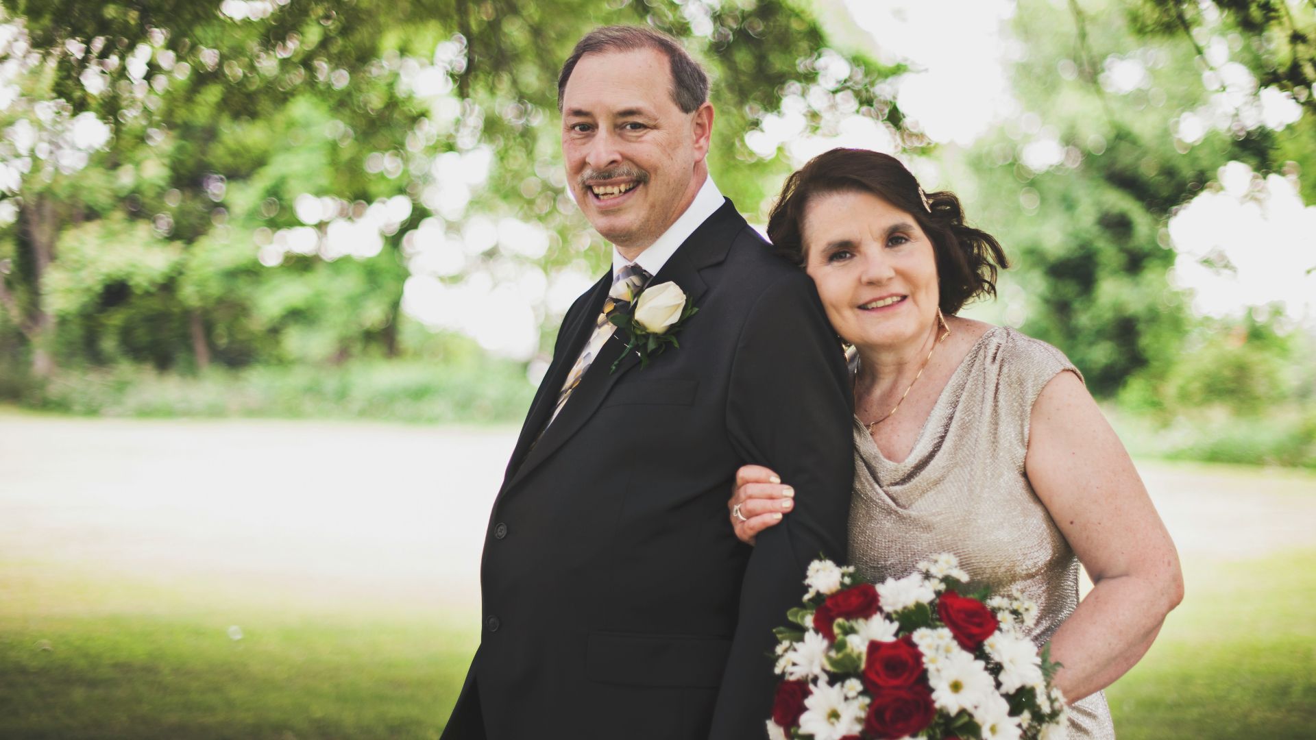 man in black suit standing beside woman in gray sleeveless dress holding bouquet of flowers