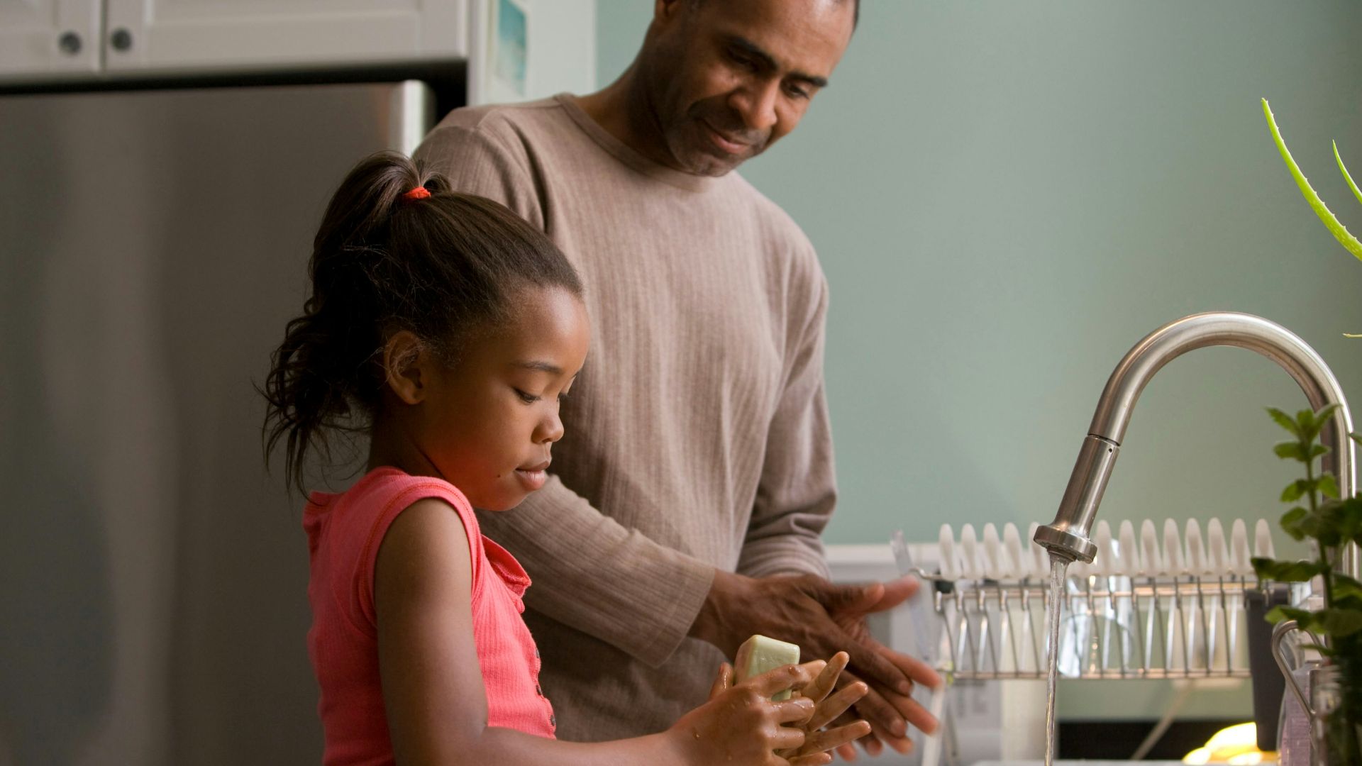 man in long sleeve shirt standing beside girl in pink tank top washing hands