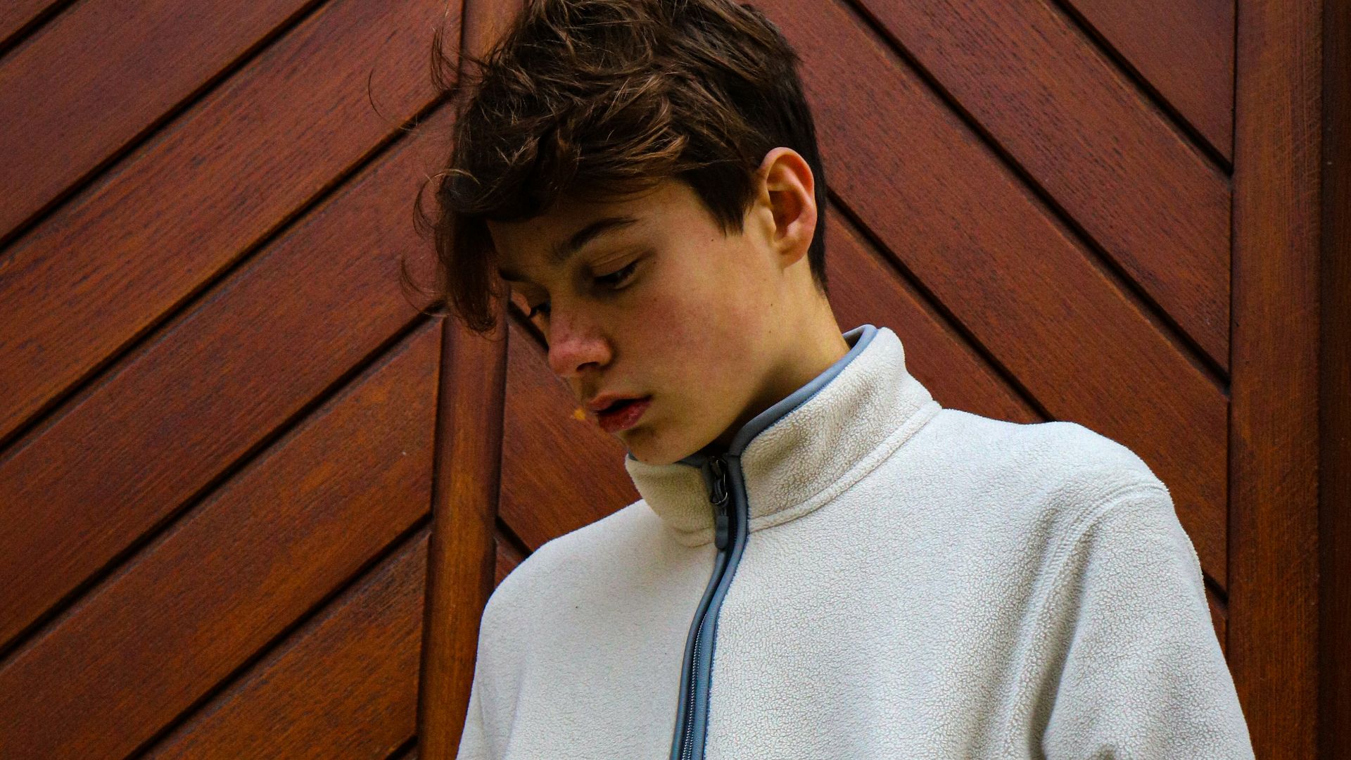 man wearing gray jacket beside brown wall