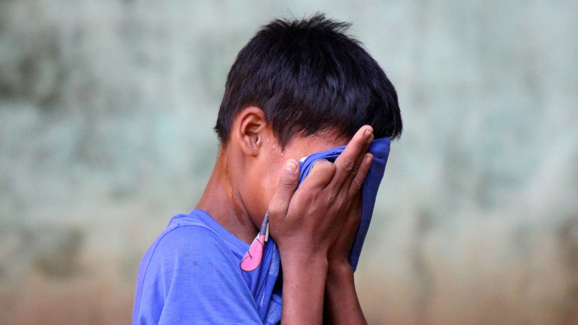 boy in blue shirt covering his face