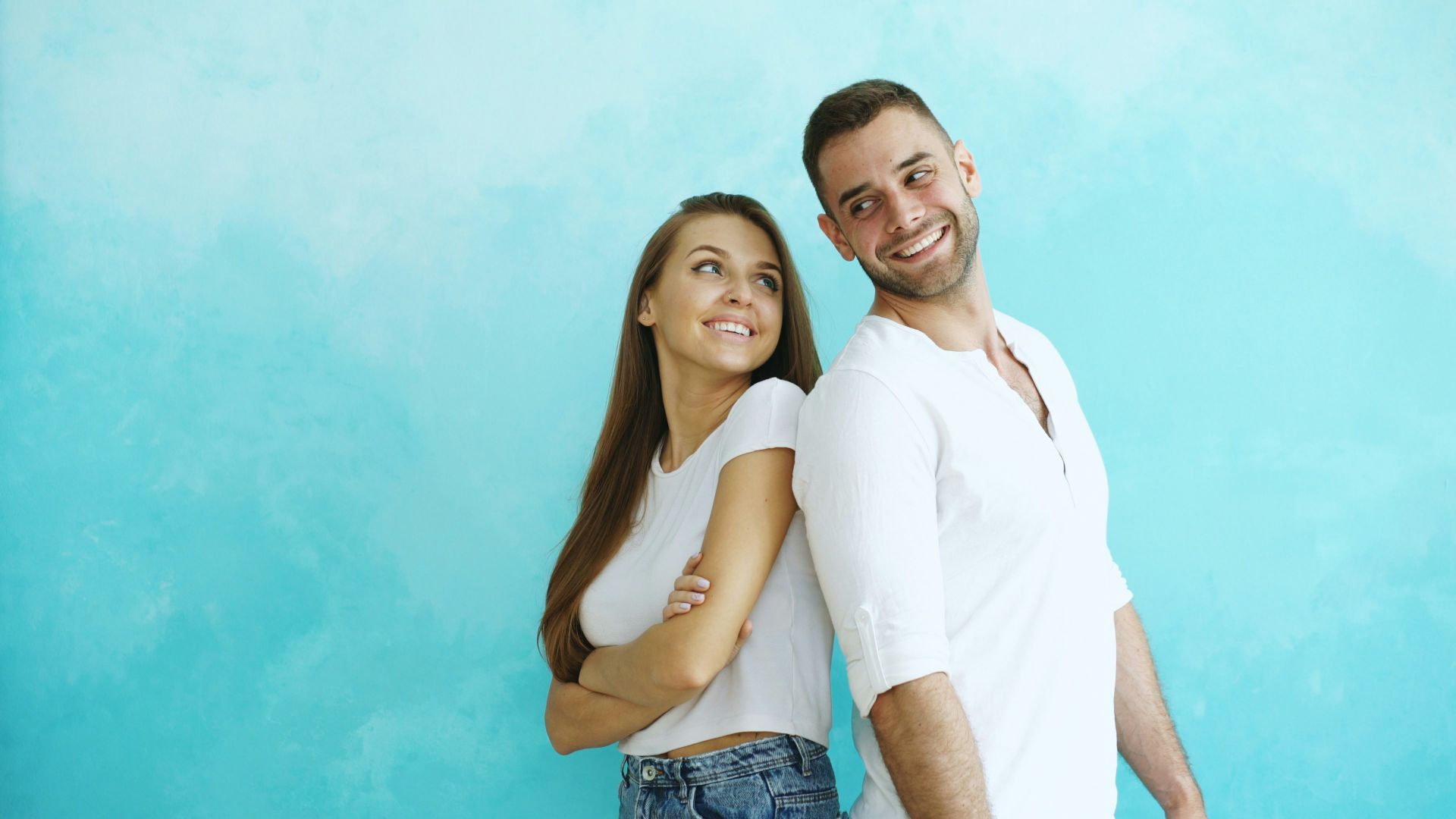 Couple smiling back to back against blue wall