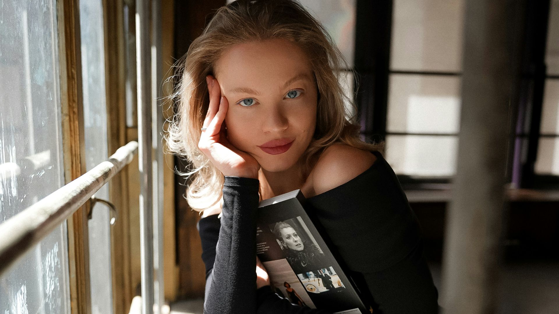 a woman leaning against a window with a book in her hand