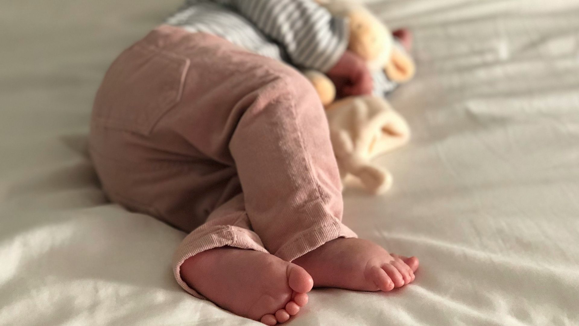 baby in gray and white striped long sleeve shirt and pink pants lying on white bed