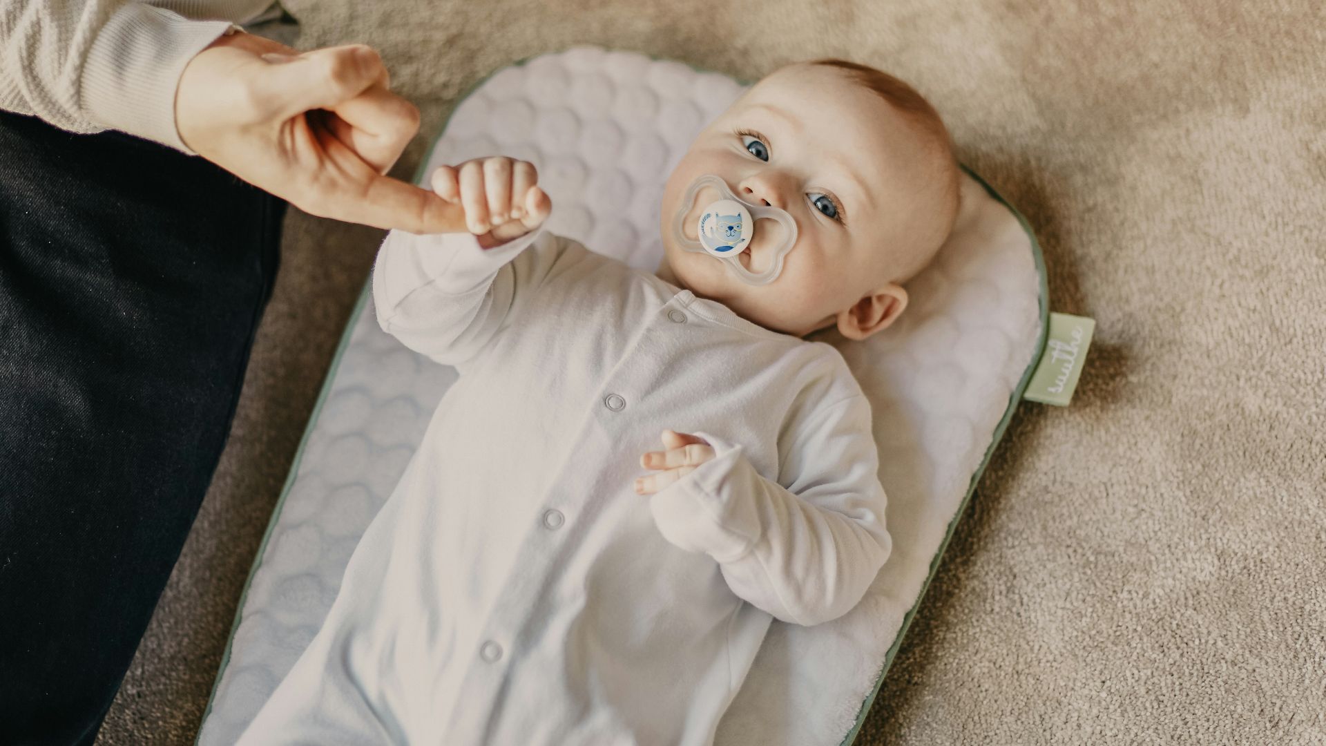 baby in white onesie lying on white textile