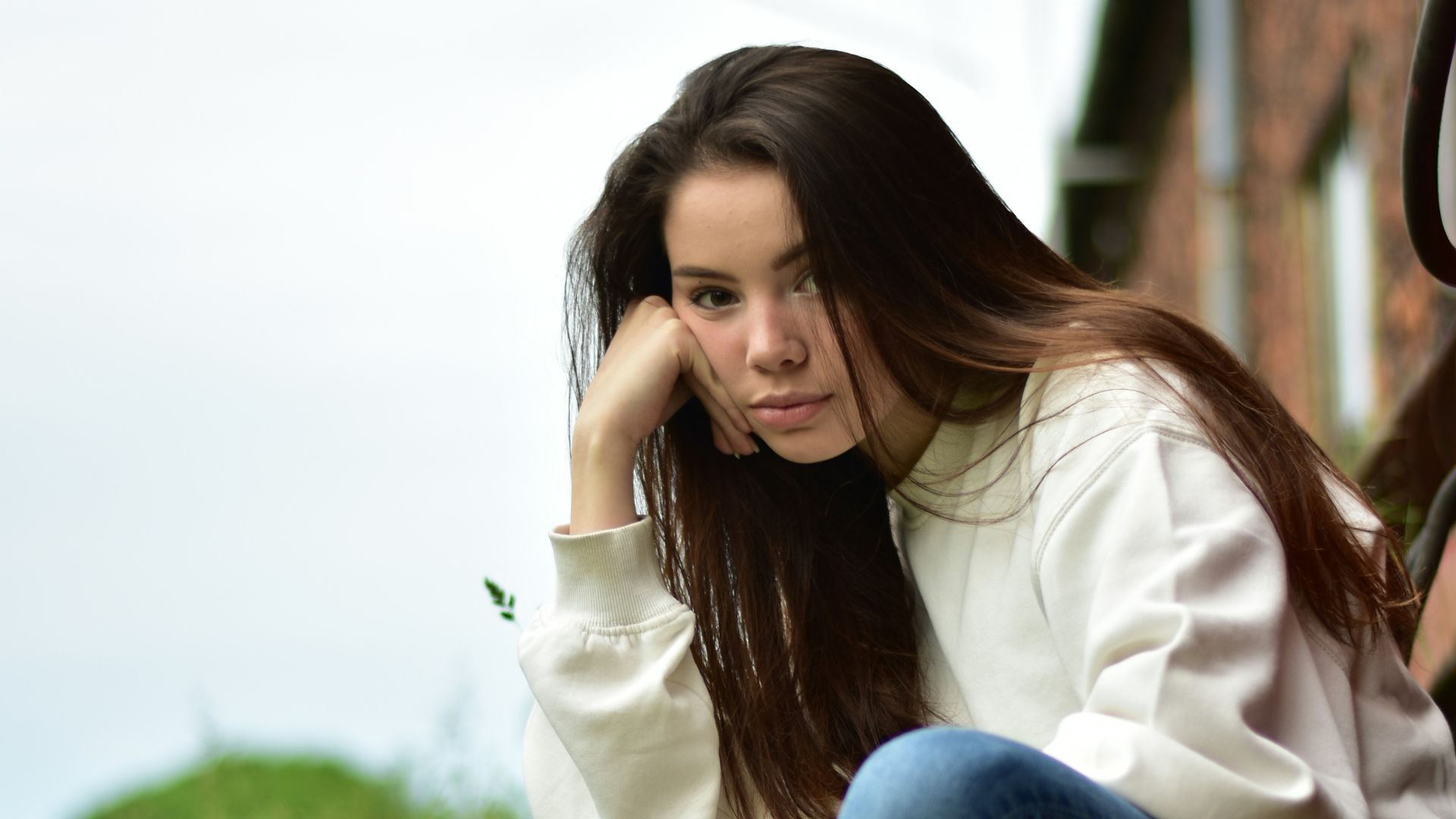 woman in white long sleeve shirt and blue denim jeans sitting on green grass during daytime