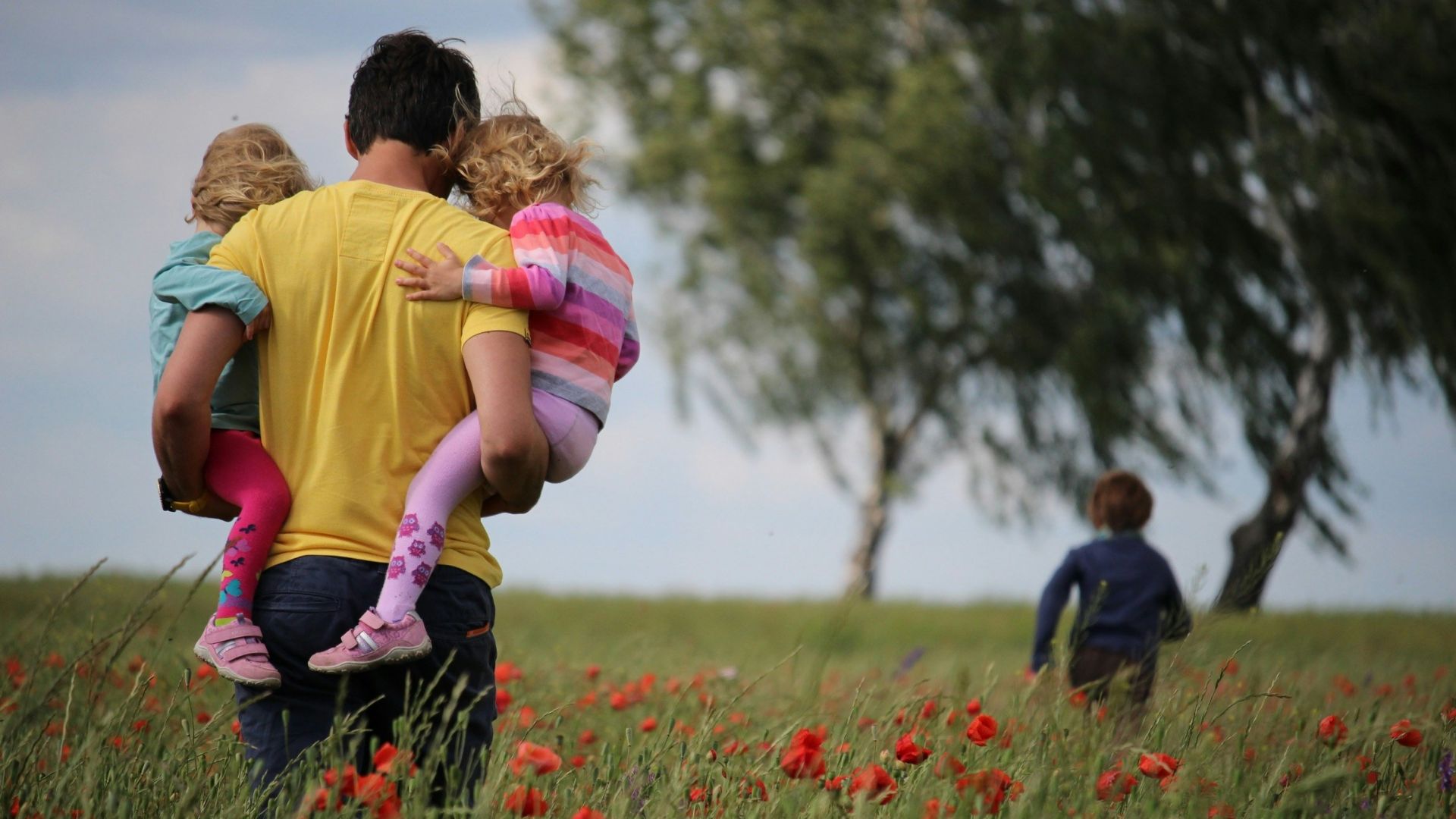 man carrying to girls on field of red petaled flower