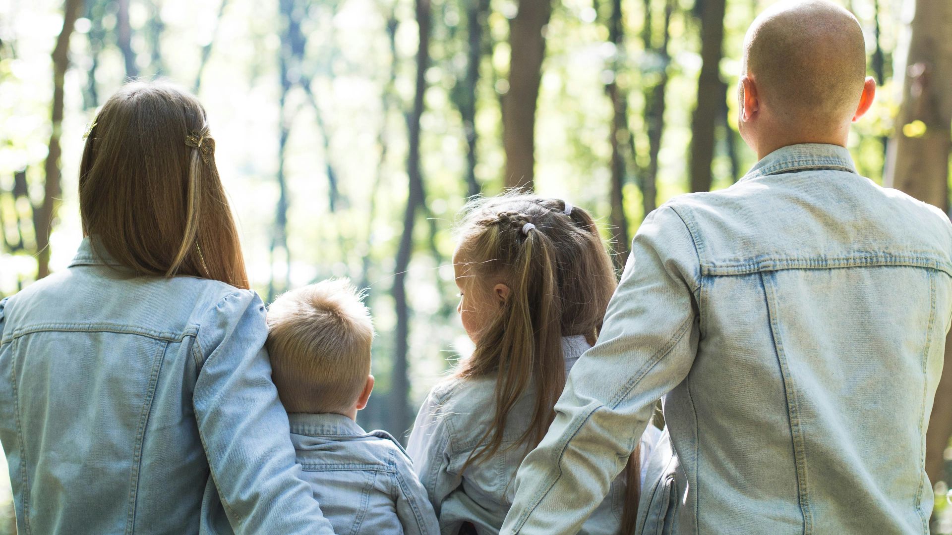 man and woman holding hands together with boy and girl looking at green trees during day