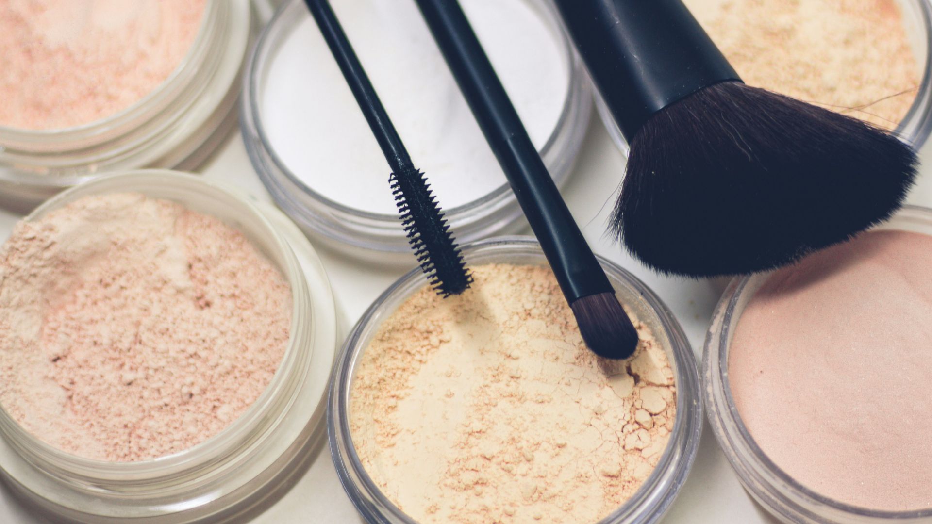 three makeup brushes on top of compact powders