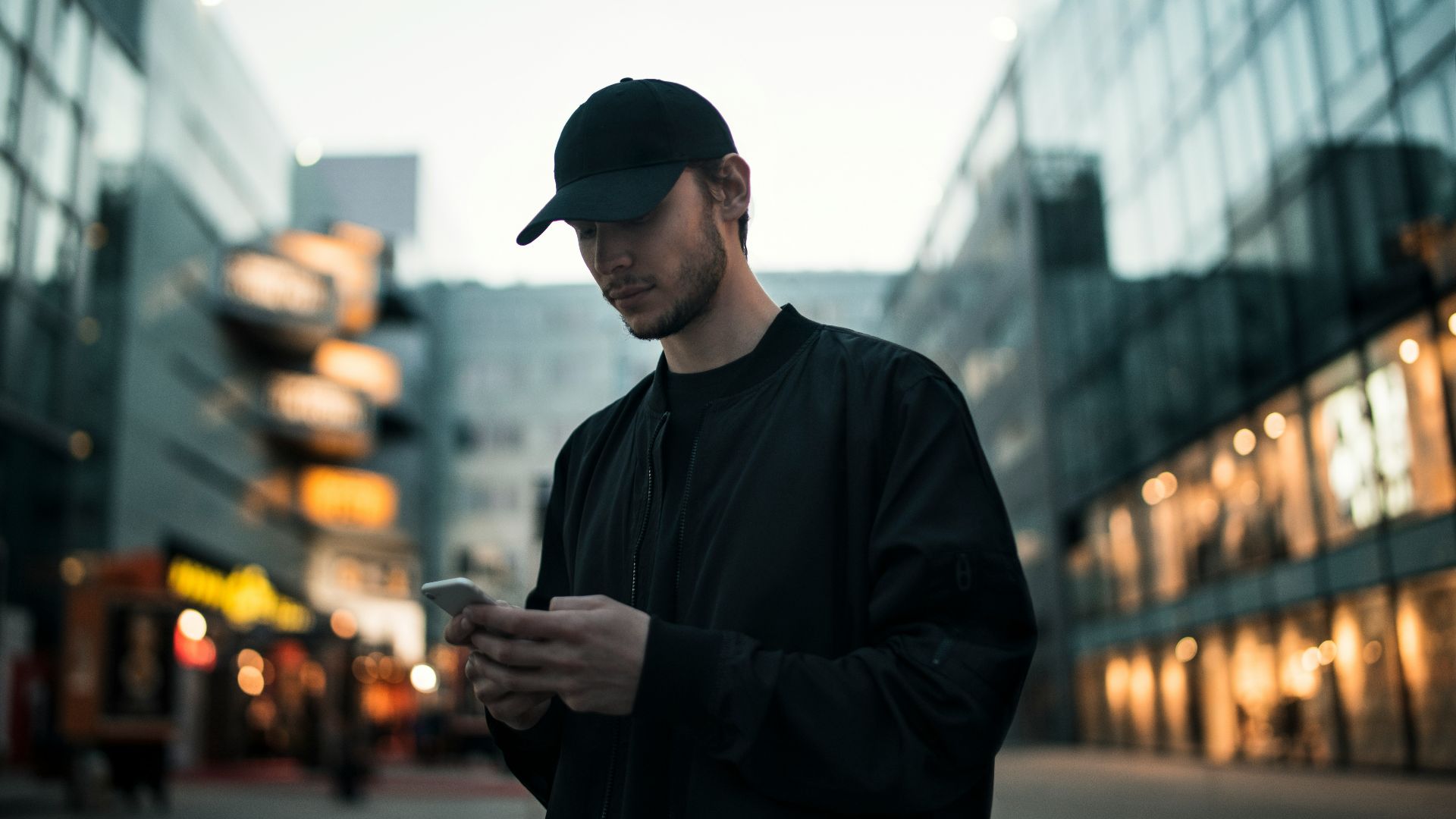 man in black jacket wearing black fitted cap while using phone