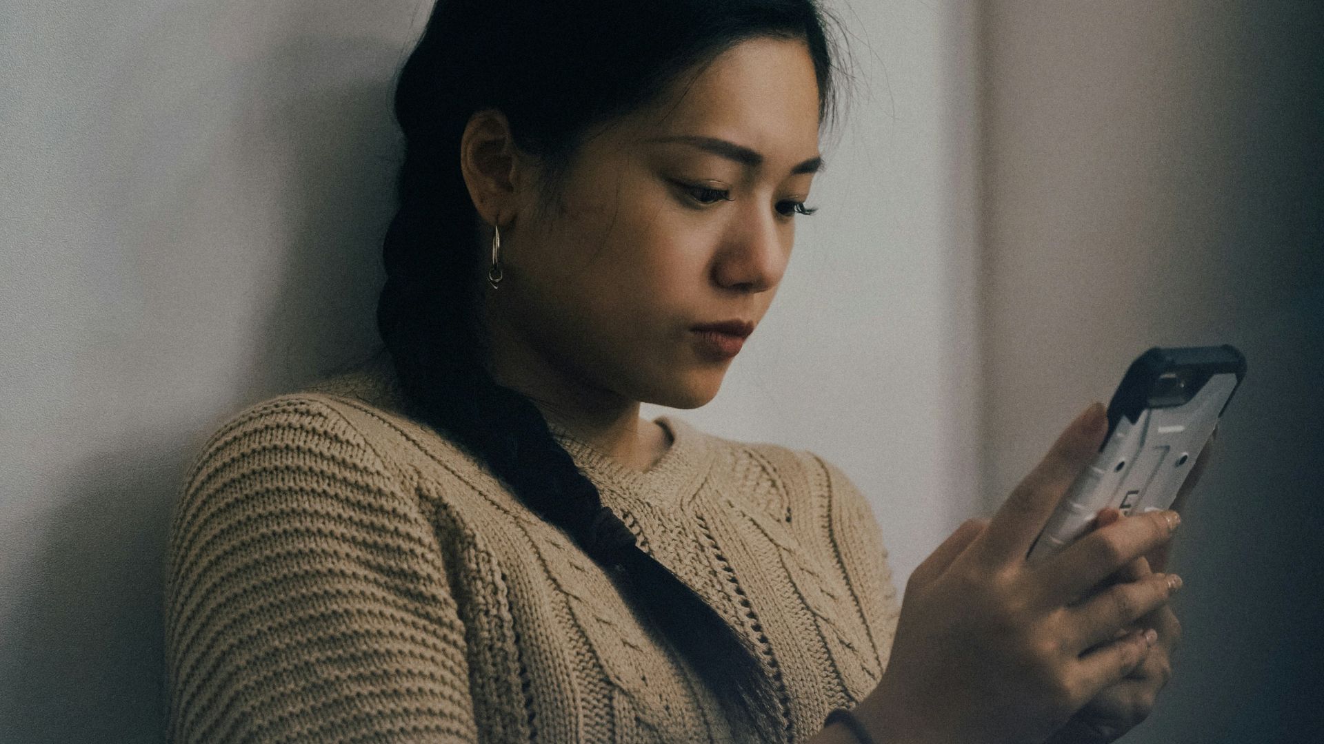 woman leaning back on white wall and using smartphone