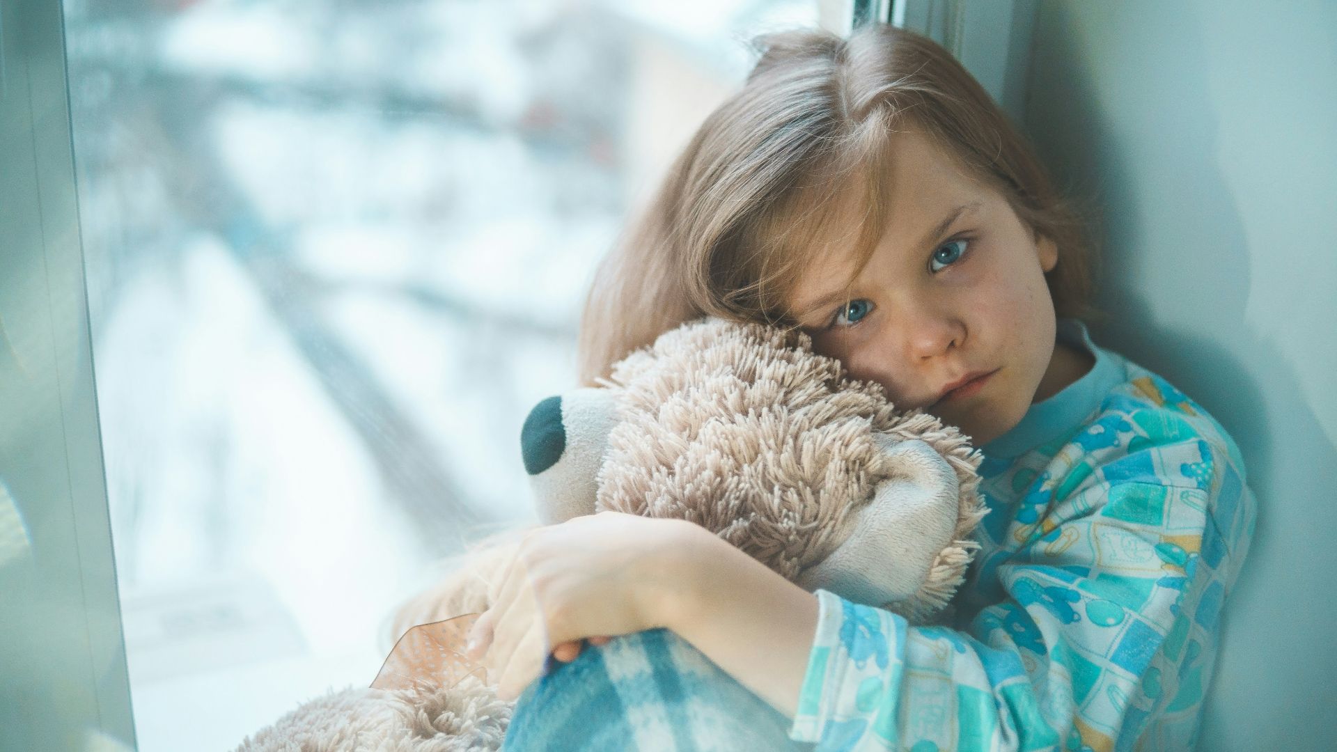 girl in blue white and red plaid shirt hugging brown teddy bear