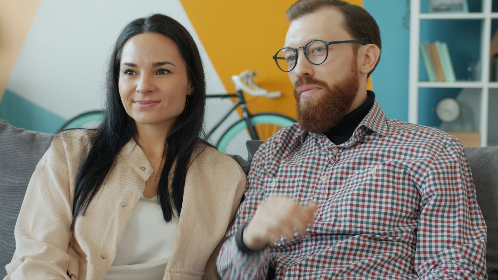 Couple sitting on a couch watching something.