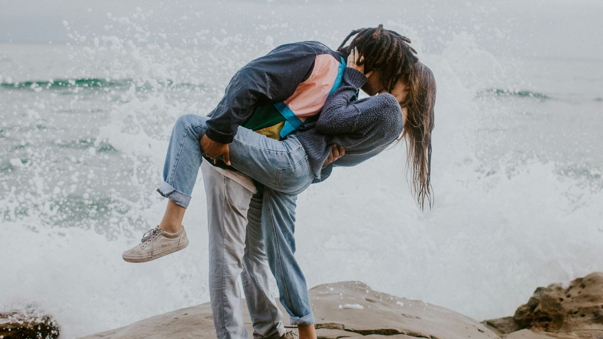 woman in blue jacket and gray pants carrying woman in blue jacket on beach during daytime