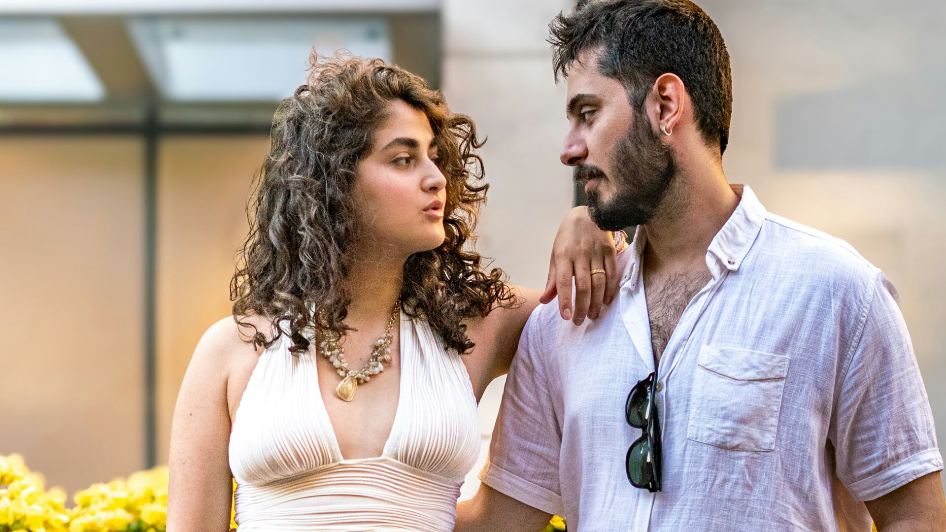 A couple poses together outdoors, looking at each other.