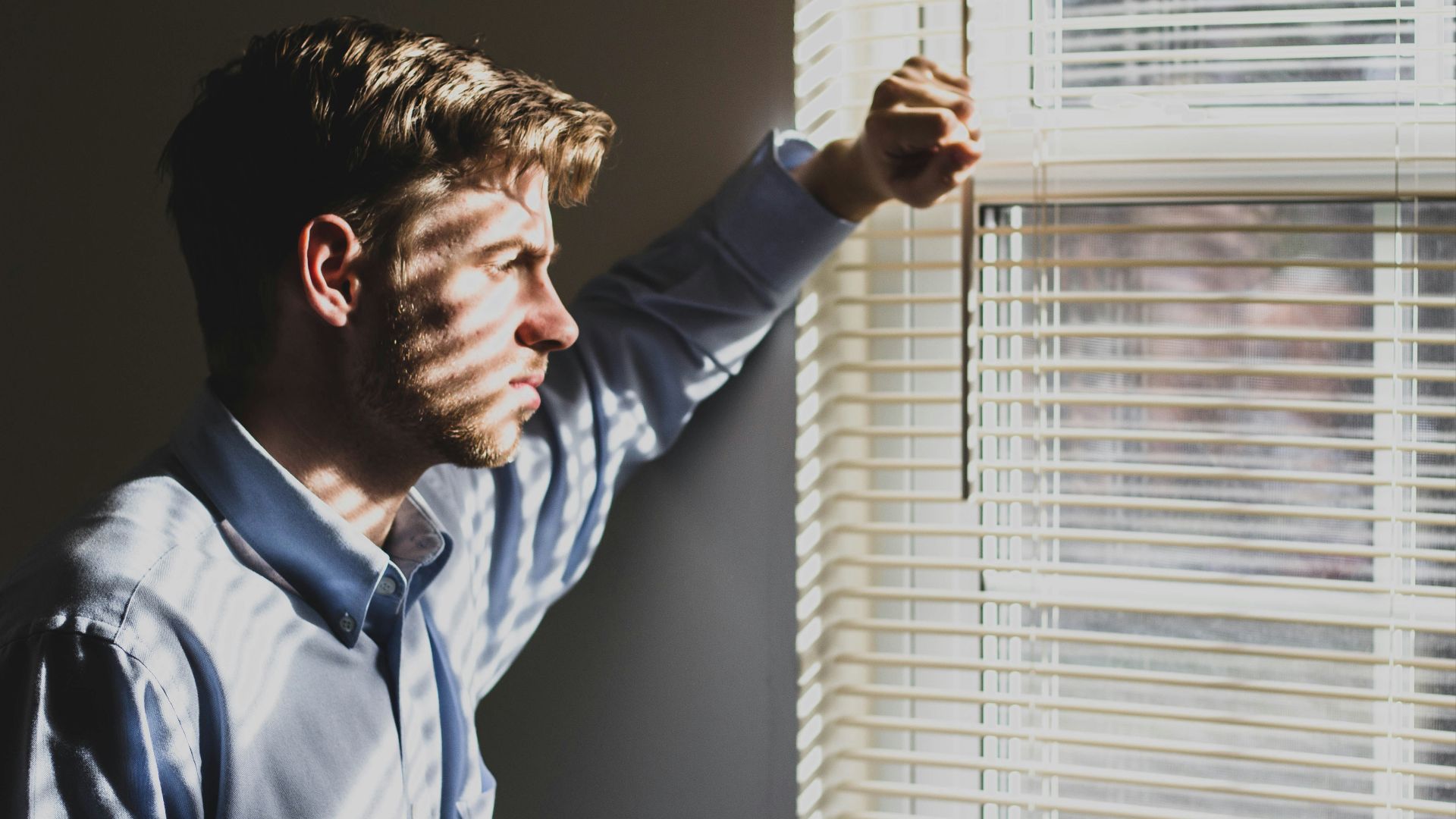 person near clear glass window pane and window blinds low-light photography