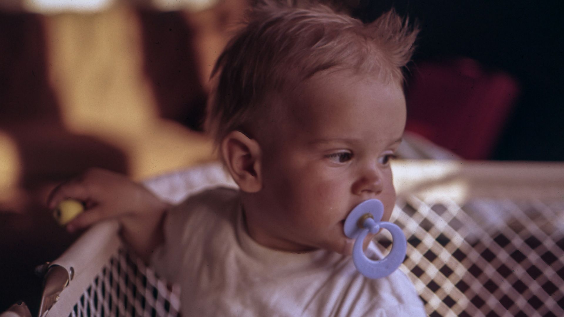 baby with purple pacifier standing on crib