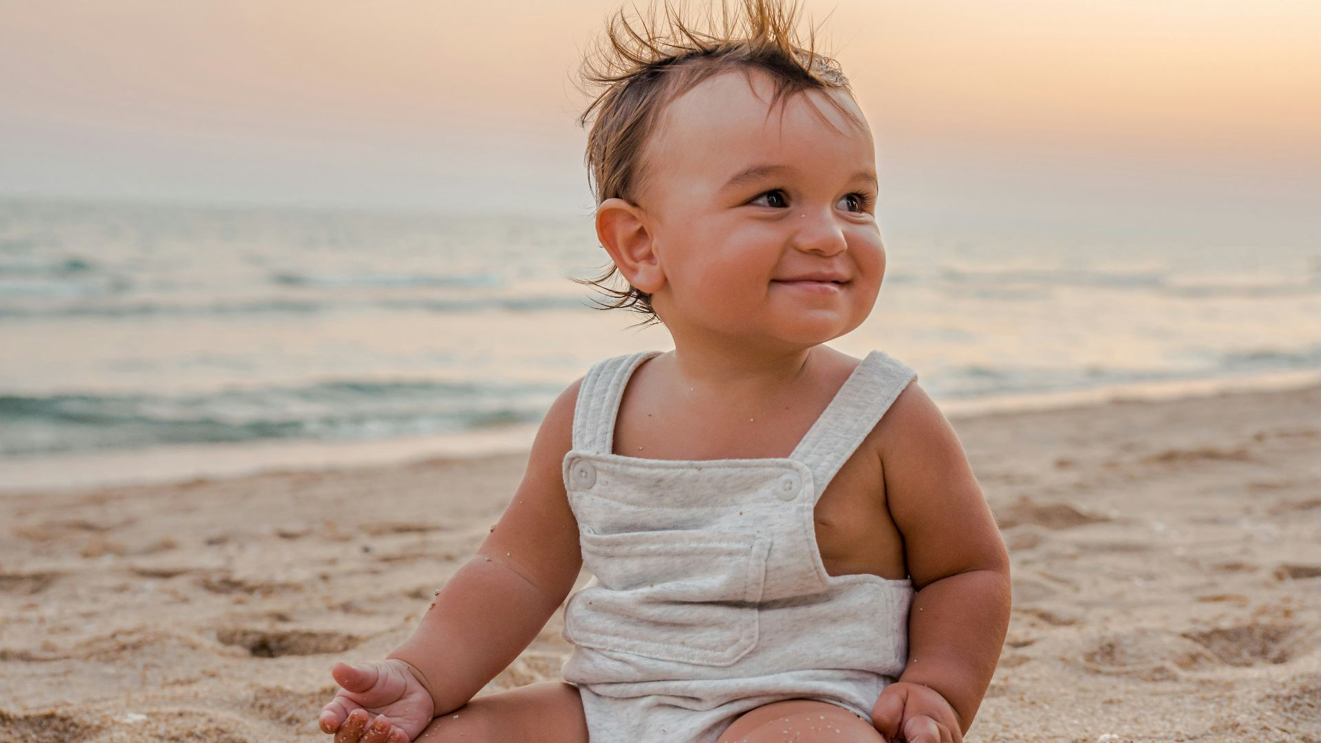 a baby sitting in the sand at the beach