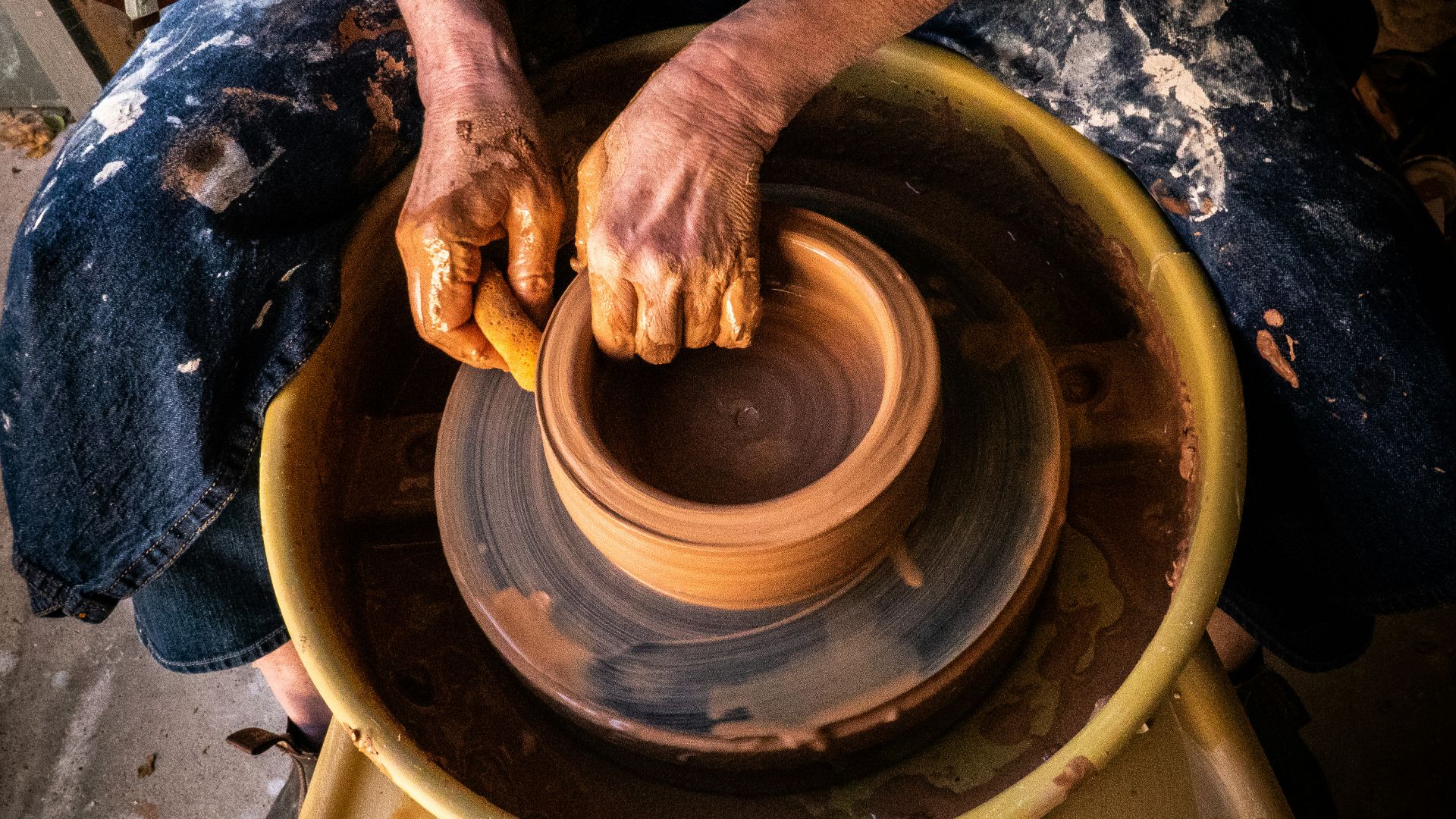 person in blue denim jeans making clay pot