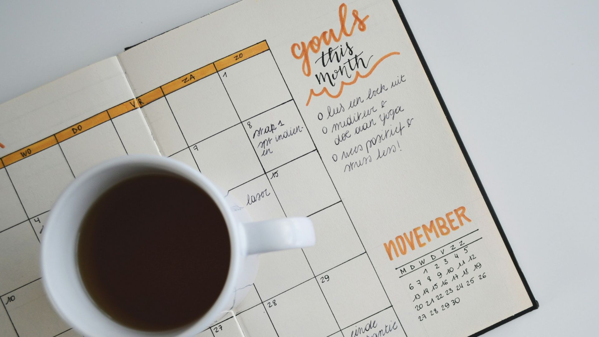 white ceramic mug with coffee on top of a planner