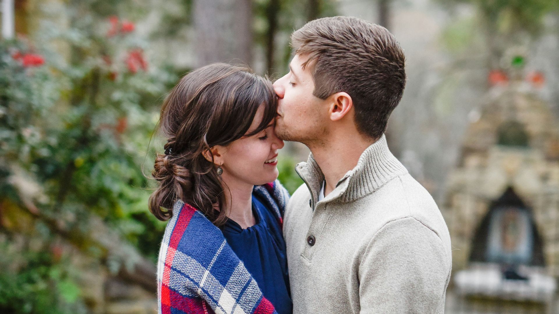 man kissing on woman forehead standing near tree during daytime