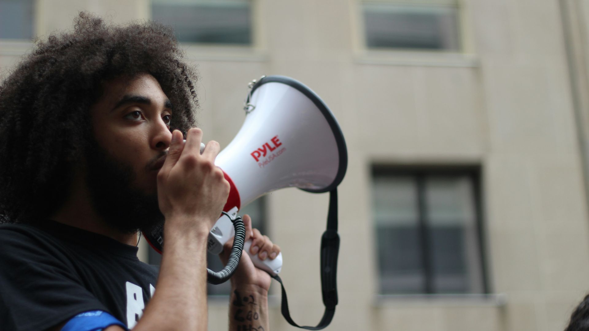 selective focus photography of man holding loudspeaker beside building