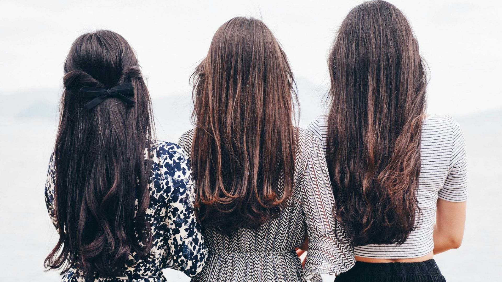 three woman looking back and facing body of water