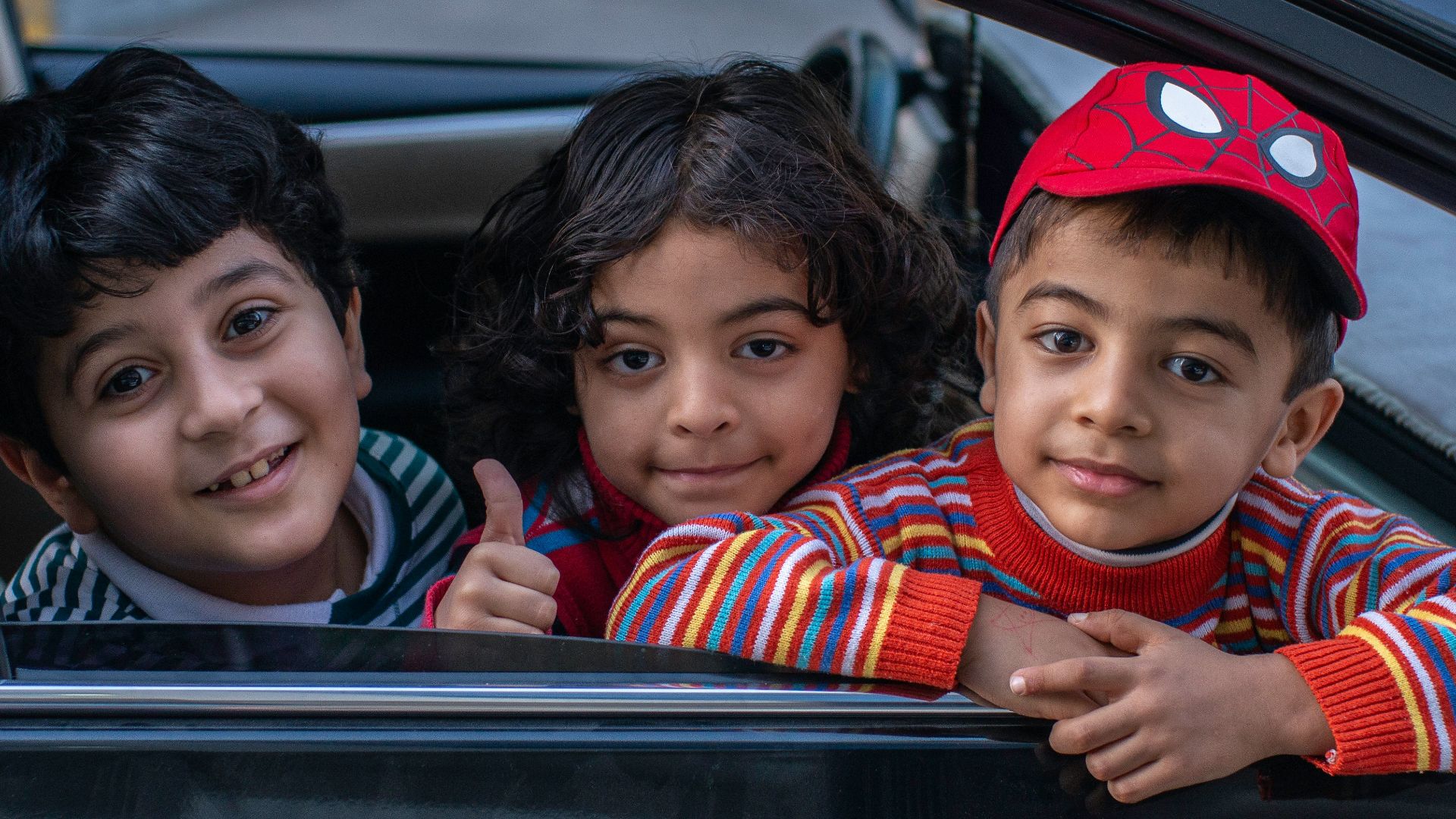 three boys looking outside window of car front seat