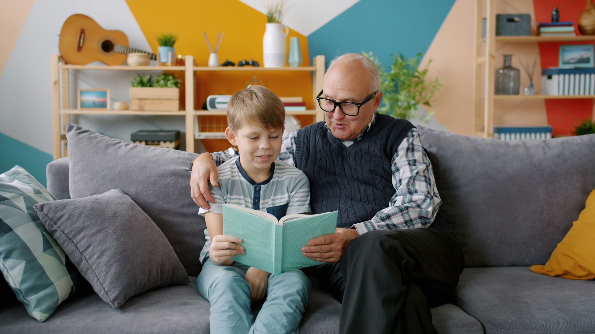 Grandfather and grandson reading a book together on couch.