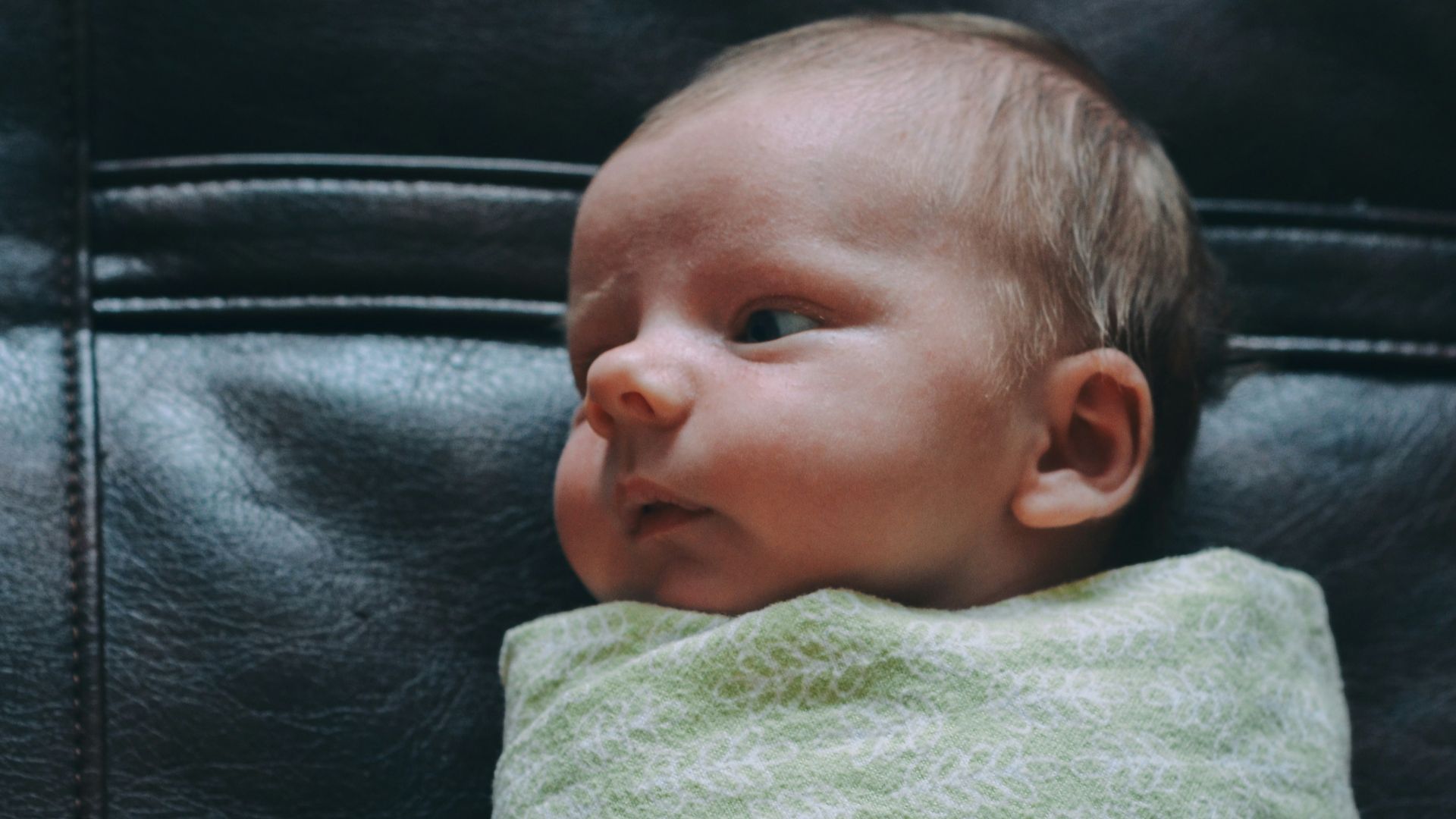baby covered in green blanket on black leather surface